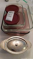 Three nested Pyrex glass baking dishes with two Pyrex glass storage containers with red lids placed on top, along with an oval stainless steel serveware dish with lid