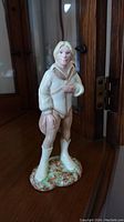 Front view of Royal Doulton china figurine showing character with light hair and clothing, standing on a textured base.