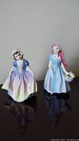 Two Royal Doulton figurines on display; left is Dinky Do in pastel dress, right is Wendy with basket of flowers