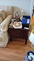 End table placed beside a sofa with various items on top (not included). Two drawers visible with brass-tone metal handles.