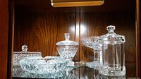 Crystal butter dish with lid, sugar bowl with lid, ashtray, and glass container displayed on glass shelf