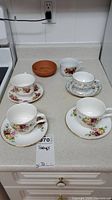 Four bone china teacups and saucers on kitchen counter, each with distinctive floral patterns and gold trim.