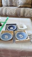 Four dishes on a table: three blue Wedgwood Jasperware trinket dishes with white classical relief and one white Royal Adderley floral ashtray.