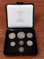 Top view of open black display case showing seven Canadian coins from 1975 in individual slots, white padded interior lid stamped with Royal Canadian Mint logos.