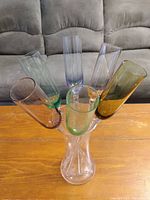 Six colored champagne flutes arranged in vase on wooden table in front of couch, top down angle showing colors and flutes