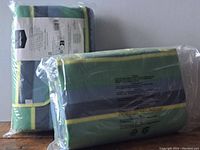 Two folded and packaged picnic blankets wrapped in plastic, displaying packaging labels on one side and the blankets' striped fabric pattern.