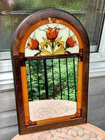 Framed decorative mirror featuring an arched stained glass panel with orange tulip flowers above rectangular mirror. Wood frame with minor wear.