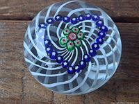 Front view of glass paperweight showing white spiral pattern, heart shaped purple star beads, and central floral bead cluster inside clear glass dome.