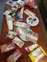 Overview of lot on wooden table including plastic cutlery, paper plates, napkins, plastic cups, and drink containers.