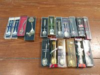 Full view of the 17 collector spoons displayed in original boxes with various packaging styles, on a wooden surface