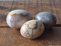 Three polished stone eggs displayed on a wooden surface showing different colors and marble patterns.
