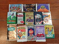 Photo showing 13 unopened trading card packs from various sports and entertainment themes including hockey, baseball, football, Star Trek, and Looney Tunes, neatly arranged on a wooden surface.