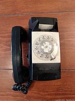 Top view of the black vintage rotary wall phone showing rotary dial, handset, and cord on wooden surface.
