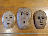 Front view of three wood carved masks with natural wood finish showing facial cutouts