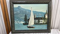 Front view of the painting showing sailboat, house, mountains, and ornate frame