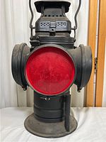 Front view of lamp showing red plastic lens centered in cast iron body with side lenses