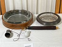 Two vintage ashtrays and two smoking pipes displayed against a curtain backdrop on a wooden surface.