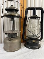 Front view of two vintage lanterns side by side against a curtain background, showing their overall shape and dimensions.