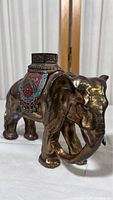 Front and side angled view of copper/brass elephant statuette showing elephant head, ears, and decorated back saddle.