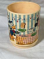 Side of cup showing Donald Duck holding toast plate and toaster on table with musical notes and blue vertical stripes background.