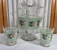 Clear glass pitcher and two matching drinking glasses with hand painted flowers on green frosted bands.