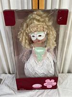 Front view of vintage blonde Gotz doll in original box wearing white mask and pastel dress.
