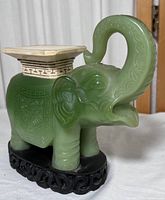 Full view of the jade-colored elephant figurine with a flat top surface and ornate black stand beneath.