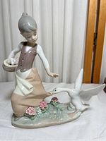 Front view of porcelain figurine showing the girl turning towards the goose with outstretched hand, basket of eggs, and floral base details.