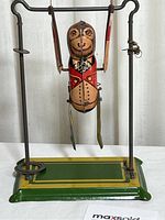 Front view of vintage metal swinging monkey toy attached to metal stand with green and yellow base.