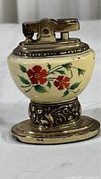 Front view of vintage Ronson Leona lighter showing porcelain body with red flower decoration and metal ornate base and lighter mechanism