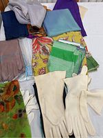 Vintage scarves and gloves laid out on a white surface showing various colors and patterns with a pair of cream and white gloves in front.
