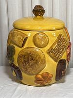 Front view of the yellow ceramic cookie jar showing various raised cookie designs and its lid with a rounded handle