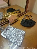 Three evening bags on table including silver mesh by Whiting & Davis, black satin bag and gold metal clutch bag