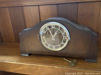 Front view of walnut mantel clock with visible key placed in front.