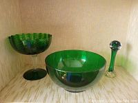 Photo showing all three green glass items together: one scalloped edge pedestal bowl, one smooth round bowl, and one bud vase with clear stem.