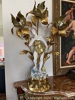 Full view of the vintage Emile Bruchon style lamp showing figure, floral base and surrounding brass flower bulbs.