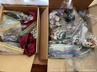 Two open cardboard boxes containing multiple plastic bags and cloth pouch bags filled with vintage buttons and sewing findings in assorted colors and styles.