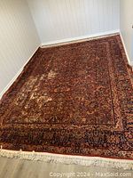 Full view of large Persian rug spread on floor showing worn areas and sewn seams of 4 pieces