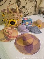 View showing all five hats and two summer bags together on a bed, illustrating the variety of styles and colors of the hats and the design details of the bags.