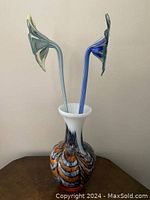 Two glass flowers in multicolored Murano-style vase on table, side view.