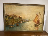 Full view of framed oil painting depicting a cliffside village and sailboats on calm water in warm brownish sepia tones.