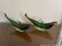 Pair of Murano glass dolphins displayed side by side on wood surface against white wall