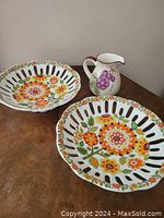 Two pierced porcelain plates and one hand-painted ceramic jug shown on wooden surface.