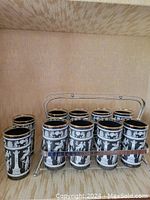 Ten Libby vintage cocktail tumblers with blue Delft Hellenic pattern and gold rims. Nine glasses arranged in a chrome metal caddy designed for eight glasses; one glass placed to the side.