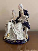 Front view of the blue and white porcelain figurine showing the Rococo couple seated and standing on a decorated base.