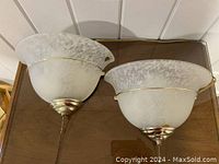 Two opal white glass wall sconces with gold metal trim and pull chains, shown on wood surface.