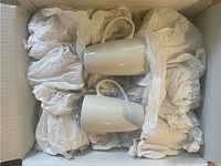 Photo showing two white ceramic mugs in a box wrapped with paper.