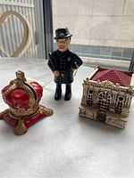 Wide shot showing all three antique metal piggy banks: crown, police officer, and bank building.