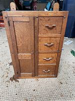 Closed view of antique wooden storage cabinet with one door and four drawers, standing on carpet.