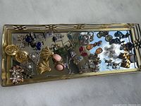 Top view of assorted earrings displayed on the brass framed mirrored tray, showing diverse styles and colors.